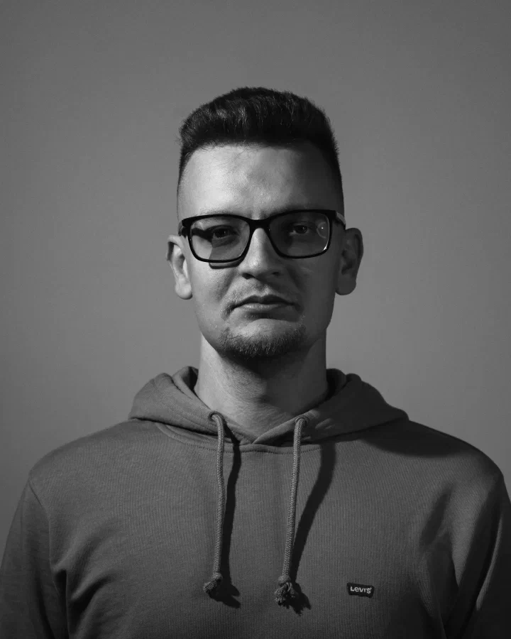 Black-and-white portrait of me in glasses and a hoodie against a plain grey wall
