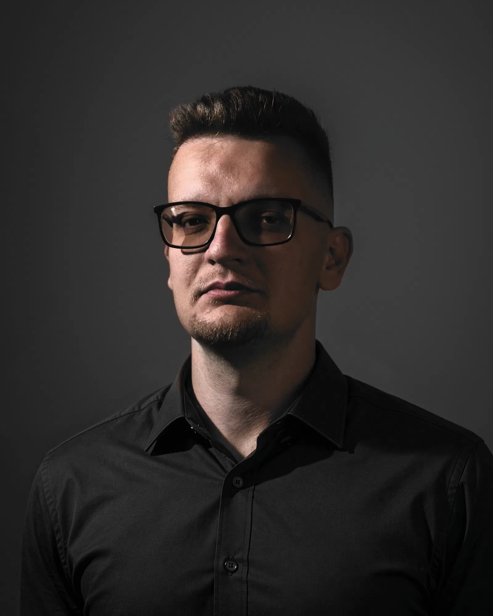 Portrait of me in glasses and a dark shirt against a dark wall